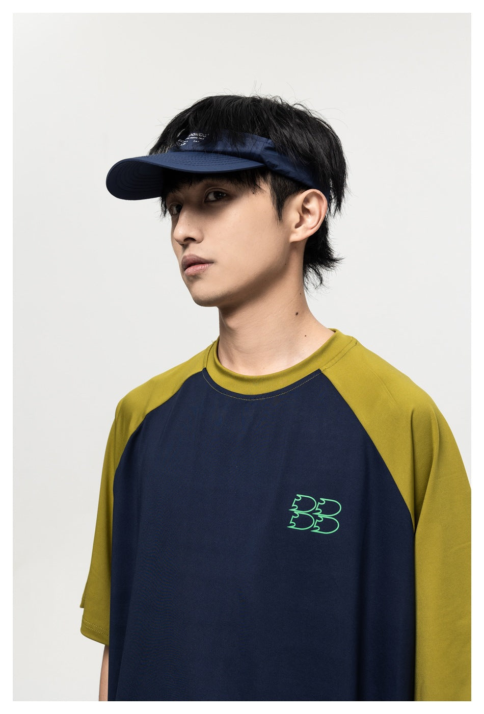 Upper-body front view of a model wearing a navy T-shirt with olive raglan sleeves and a small green chest graphic.