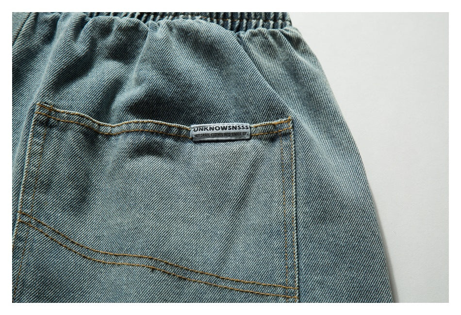 Close-up of a back pocket on light blue denim shorts with a small sewn label and tan stitching.