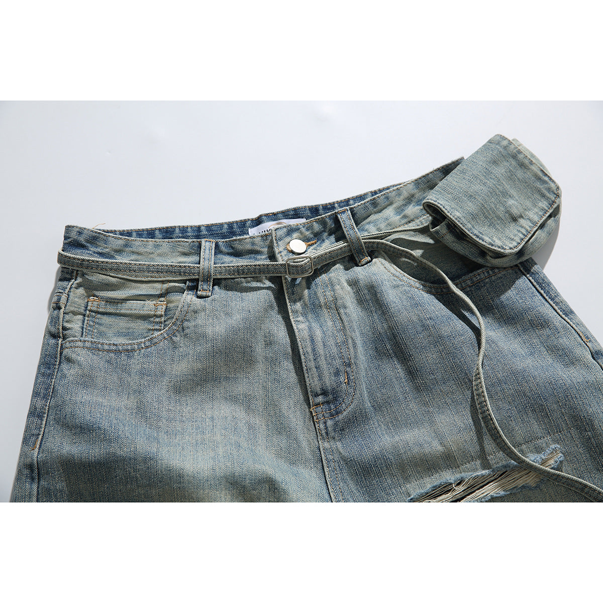 Close view of faded blue jeans with belt loops, button closure, a slim belt, attached pouch, and frayed distressing.