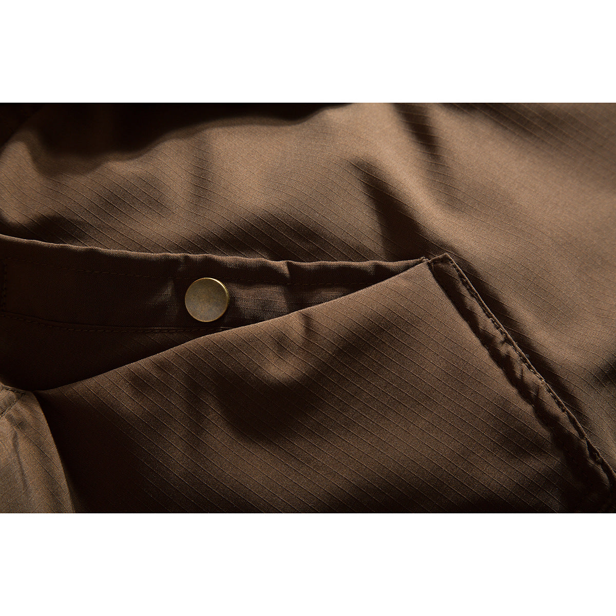 Close-up of a brown jacket pocket flap with a round snap and subtle grid-textured fabric.