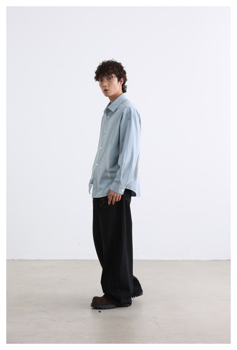 Model wearing the blue button-up shirt with brushstroke marks, shown from the side with black wide-leg jeans