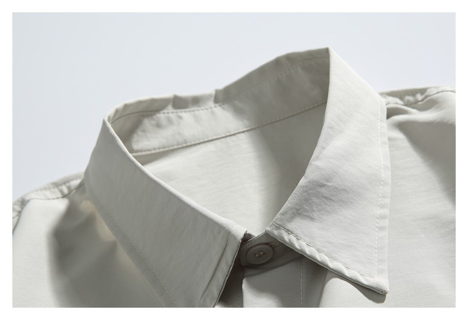 Close-up of the pointed collar and top button on a light gray shirt.