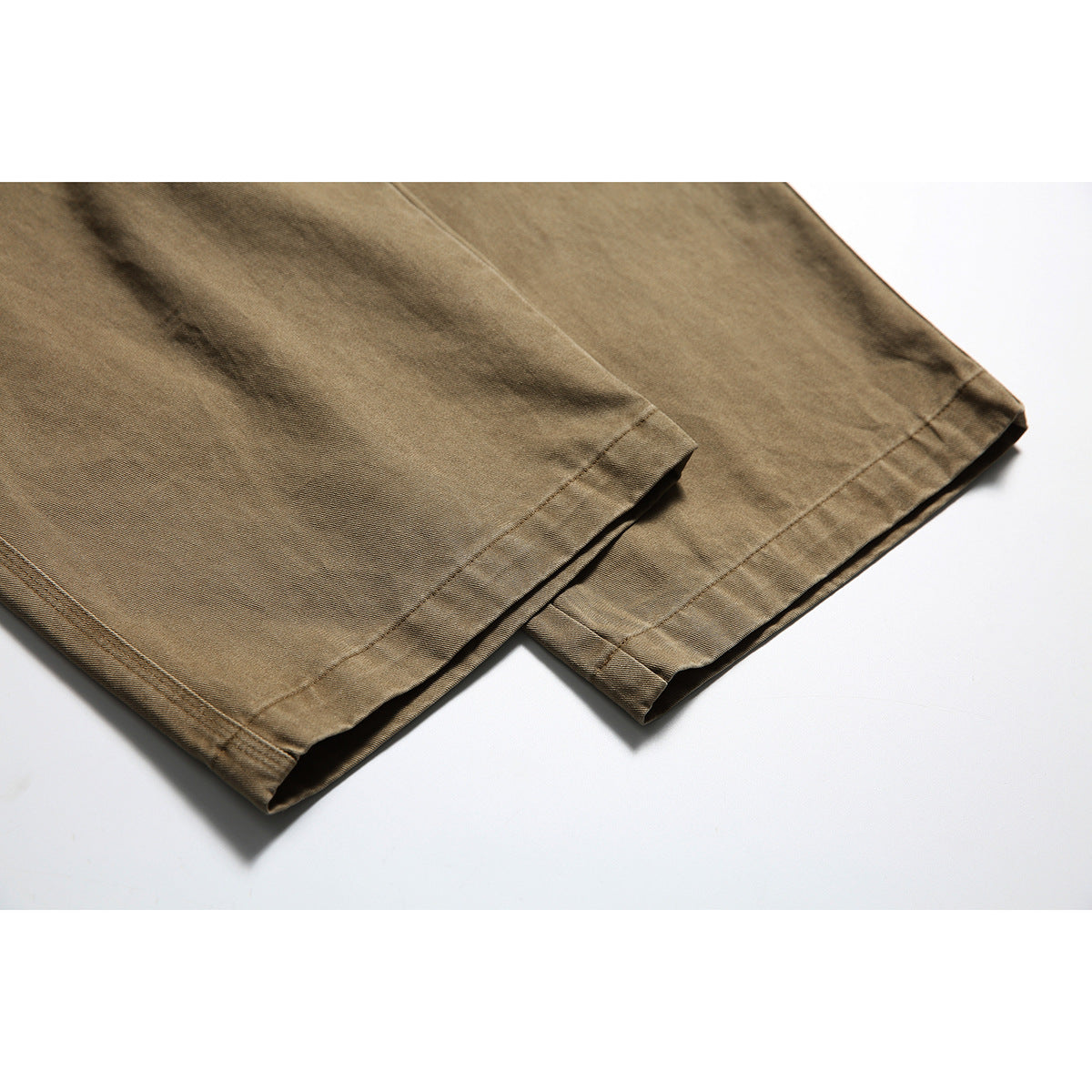 Close-up of the stitched hems on the legs of tan utility pants.