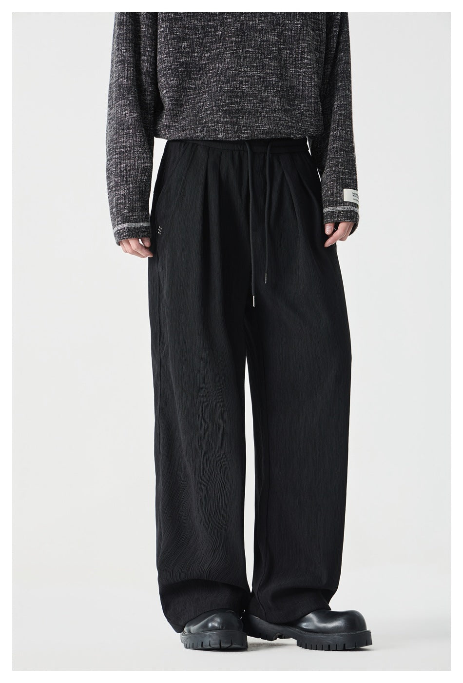 Front view of black wide-leg drawstring pants with a subtle crinkled texture, worn with a dark sweater.