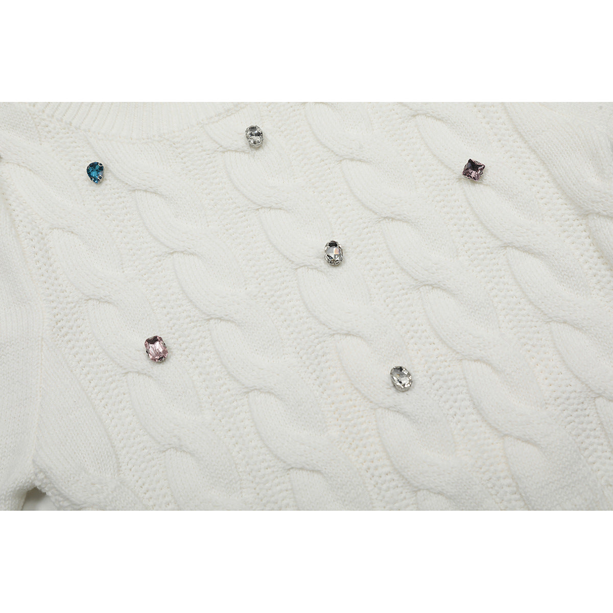 Close-up of white cable-knit sweater stitching with scattered blue, pink, and clear jeweled accents.