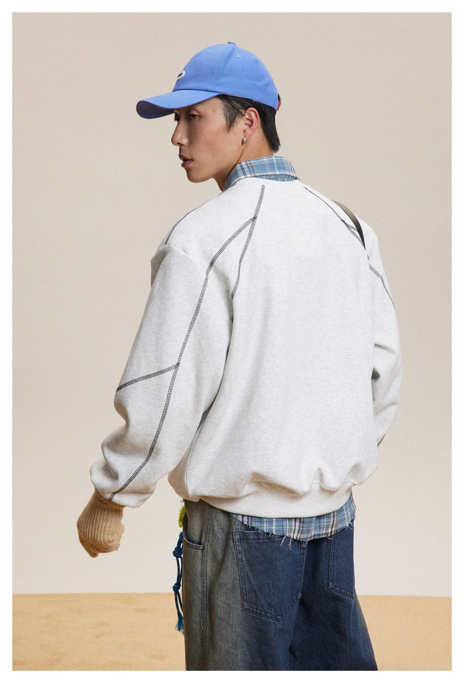 Back view of a model wearing a light gray sweatshirt with dark contrast seams and a ribbed hem.