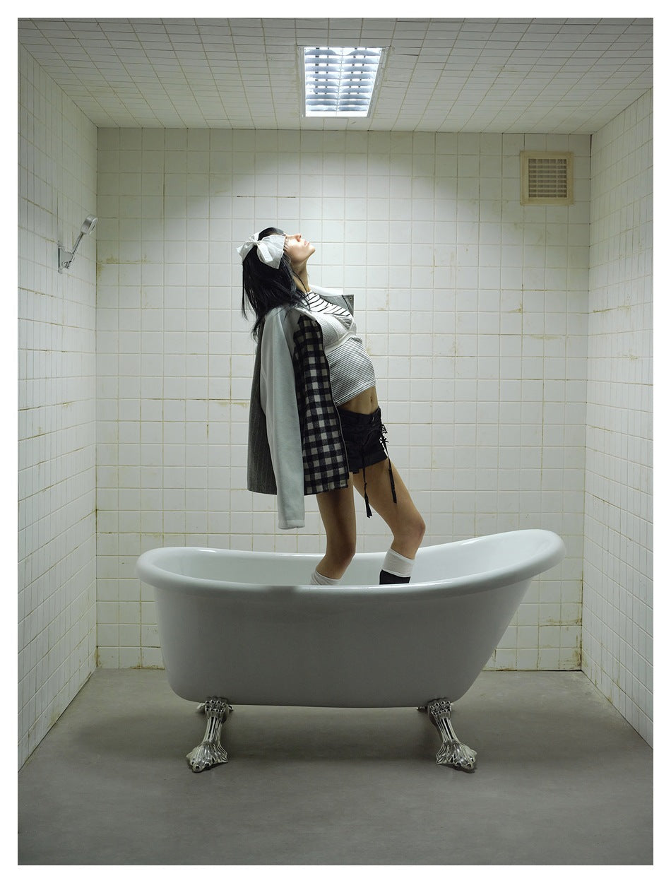 Model wearing the patchwork jacket while posing in a bathtub in a tiled room.