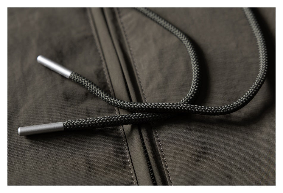 Close-up of black braided drawstrings with metal tips against a dark olive jacket.