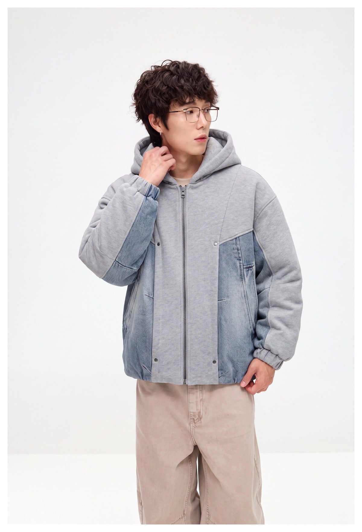 Model wearing a gray hooded zip jacket with blue denim panels and beige trousers, shown from the front at an angle.