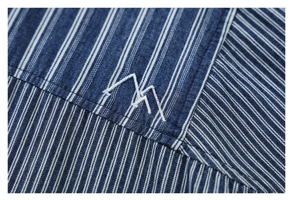 Close-up of a white angular embroidered mark on blue-and-white striped shirt fabric.