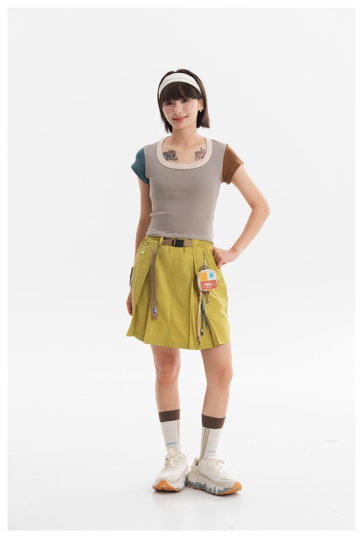 Model wearing a taupe scoop-neck top with teal and brown sleeves and a mustard skirt with a belt.