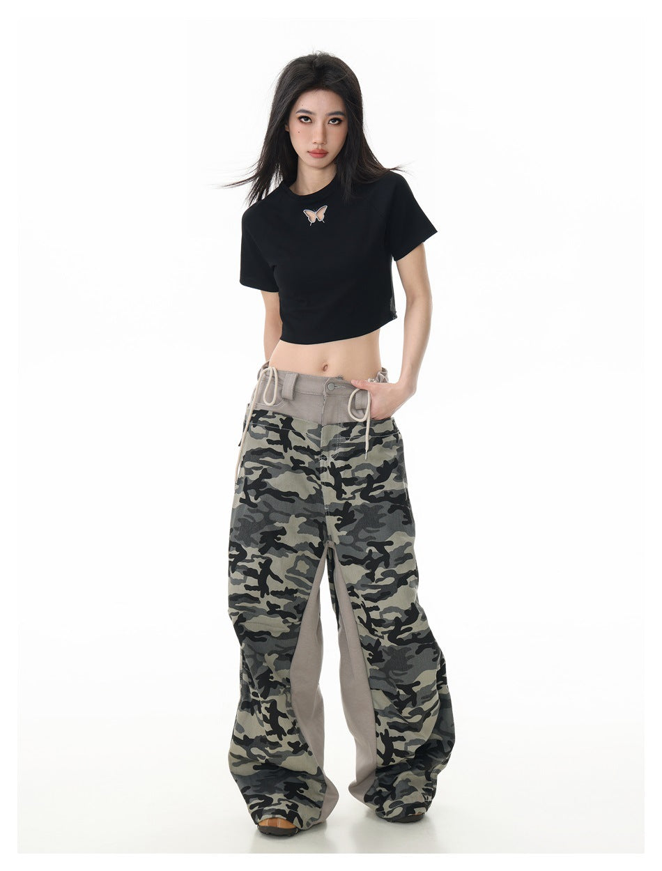 Full-length front view of a model wearing a black cropped butterfly T-shirt and wide gray camouflage pants.