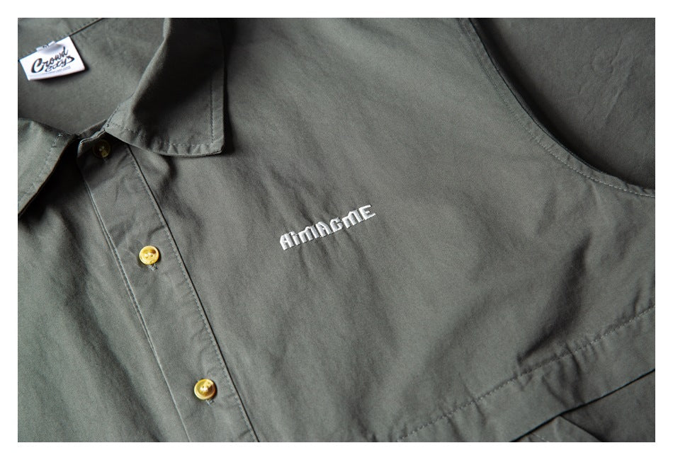 Close-up of a dark gray-green collared shirt with tan buttons and small white chest embroidery.