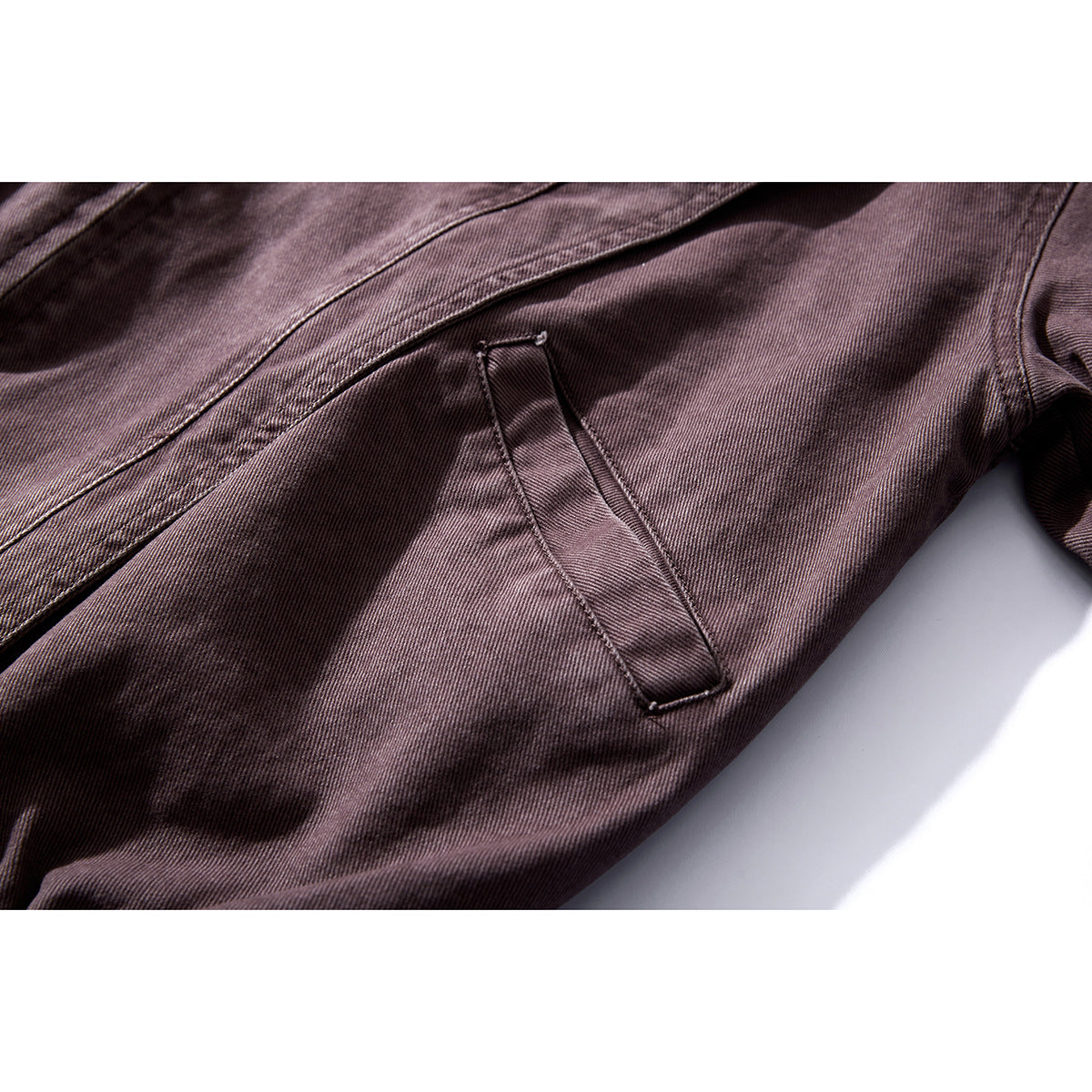 Close-up of a dark plum jacket showing a slanted welt pocket and stitched panels.