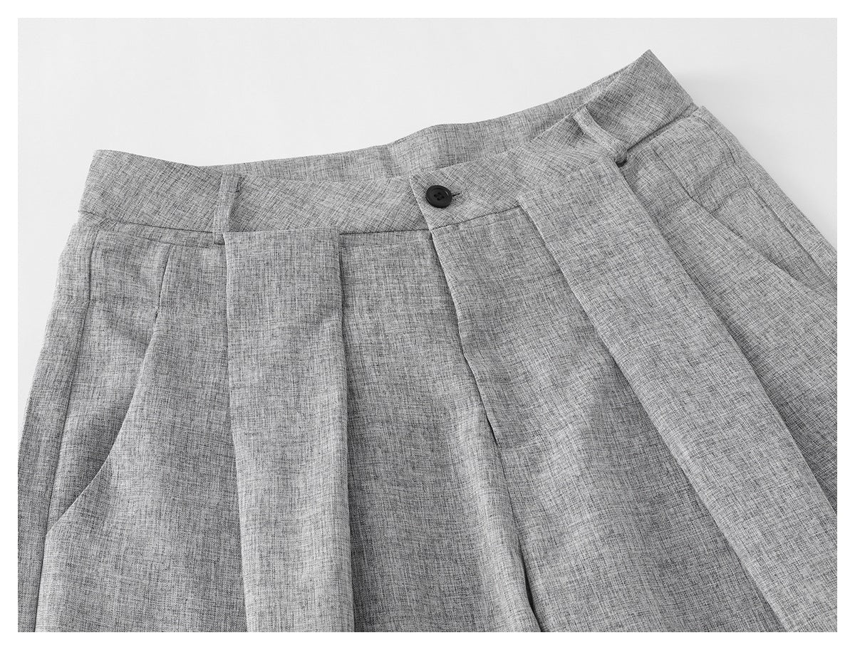 Close-up of gray wide-leg trousers showing the waistband, button, pleats, and front pocket.