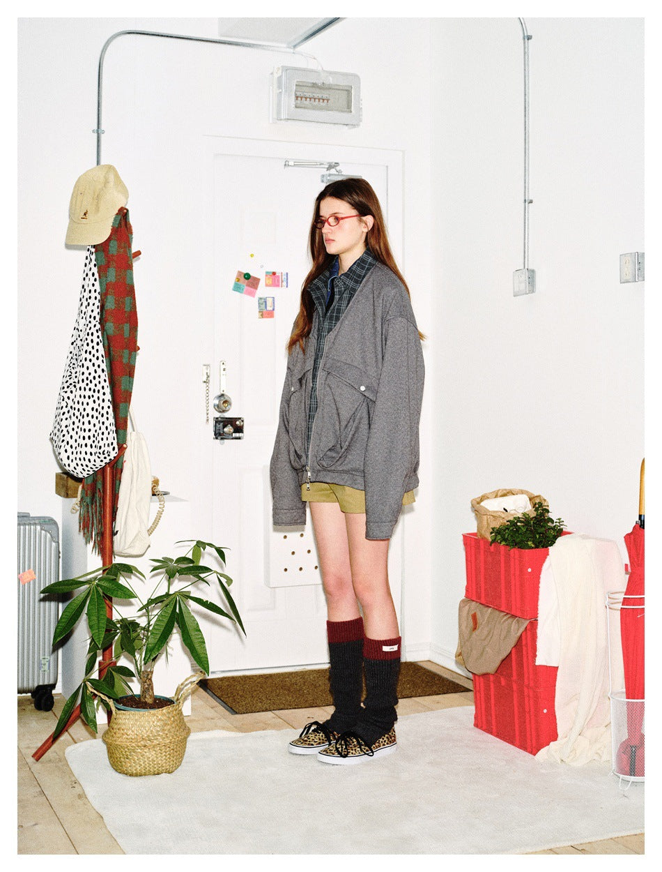 Side view of a model wearing an oversized gray jacket with plaid shirt lining, olive shorts and tall dark socks.