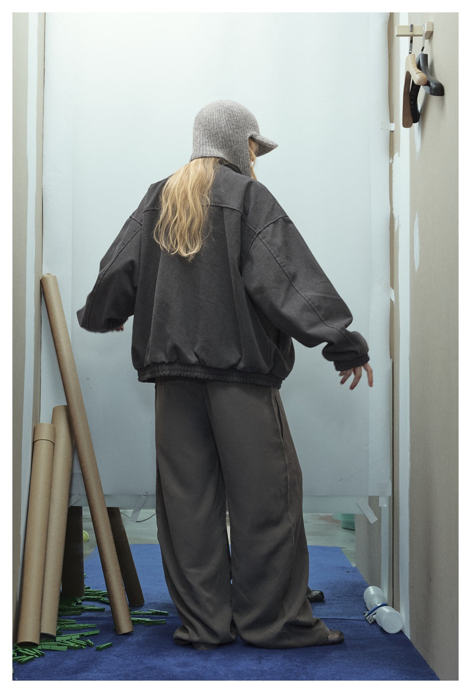 Back view of a model wearing an oversized charcoal jacket and wide-leg pants with a gray knit cap.
