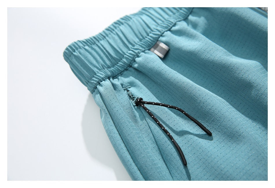 Close-up of a black zipper pull on light blue shorts, beside the elastic waistband and subtle dotted fabric texture.