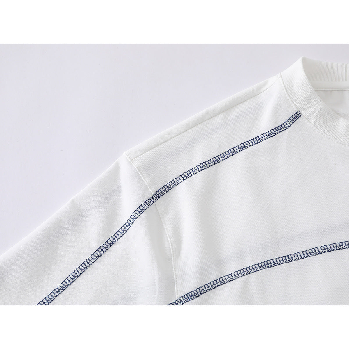 Close-up of a white T-shirt showing dark contrast overlock seams across the shoulder and chest.
