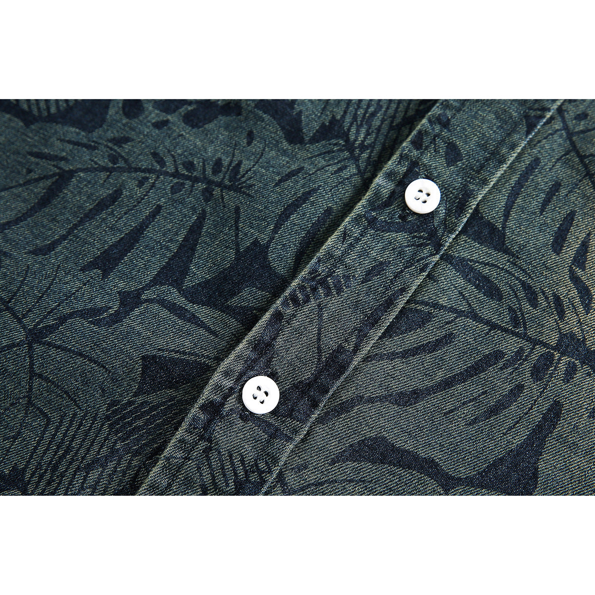Close-up of two white buttons and the dark botanical pattern on blue-gray shirt fabric.