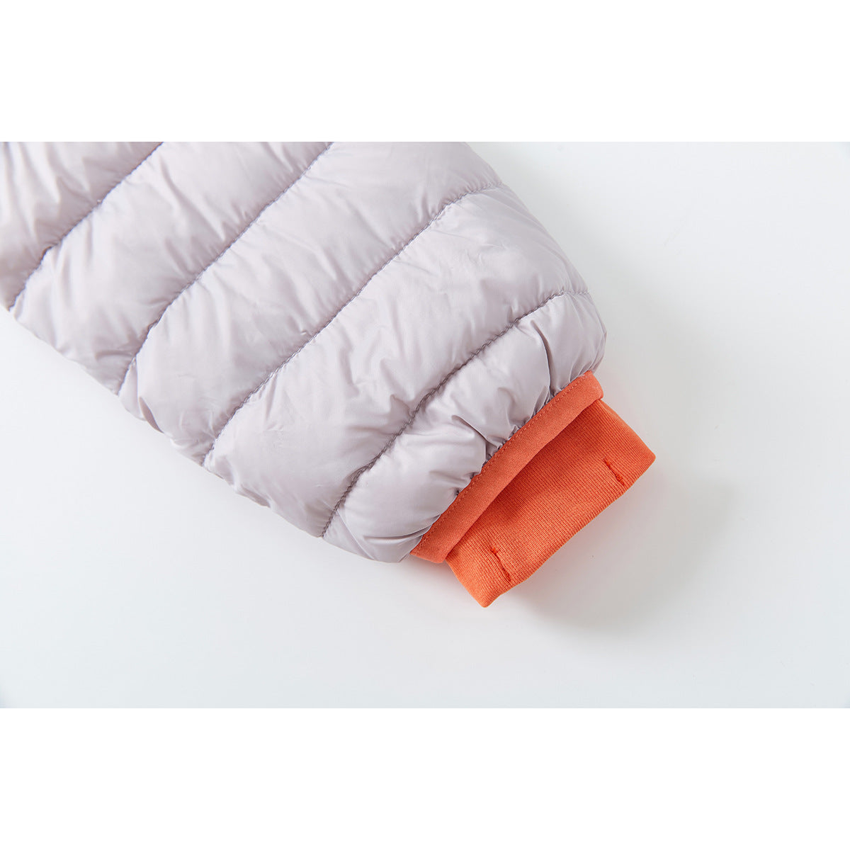 Close-up of a pale lavender quilted jacket sleeve ending in a bright orange ribbed cuff.