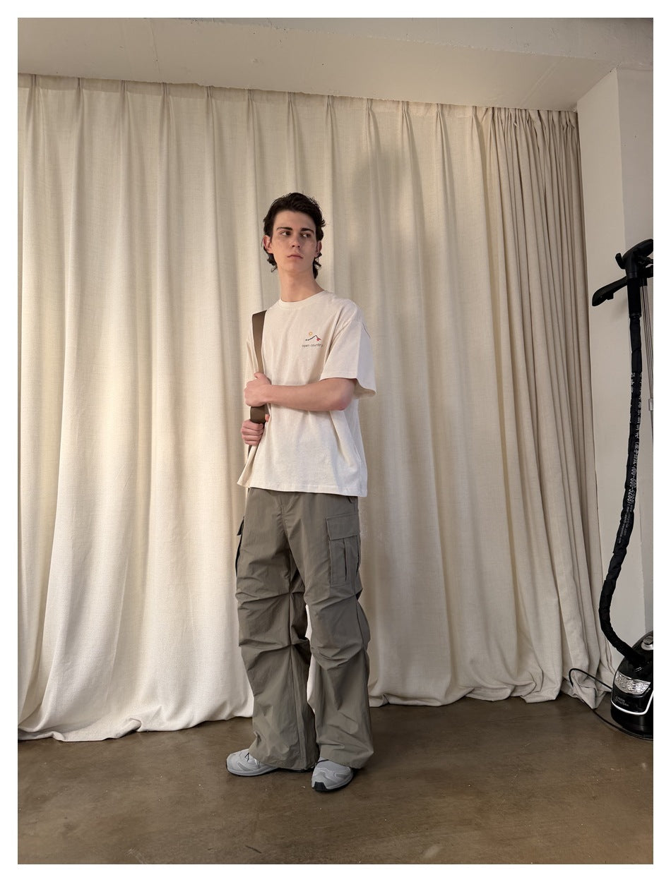 Front view of a man wearing loose gray-olive cargo pants with large thigh cargo pockets and a cream T-shirt.