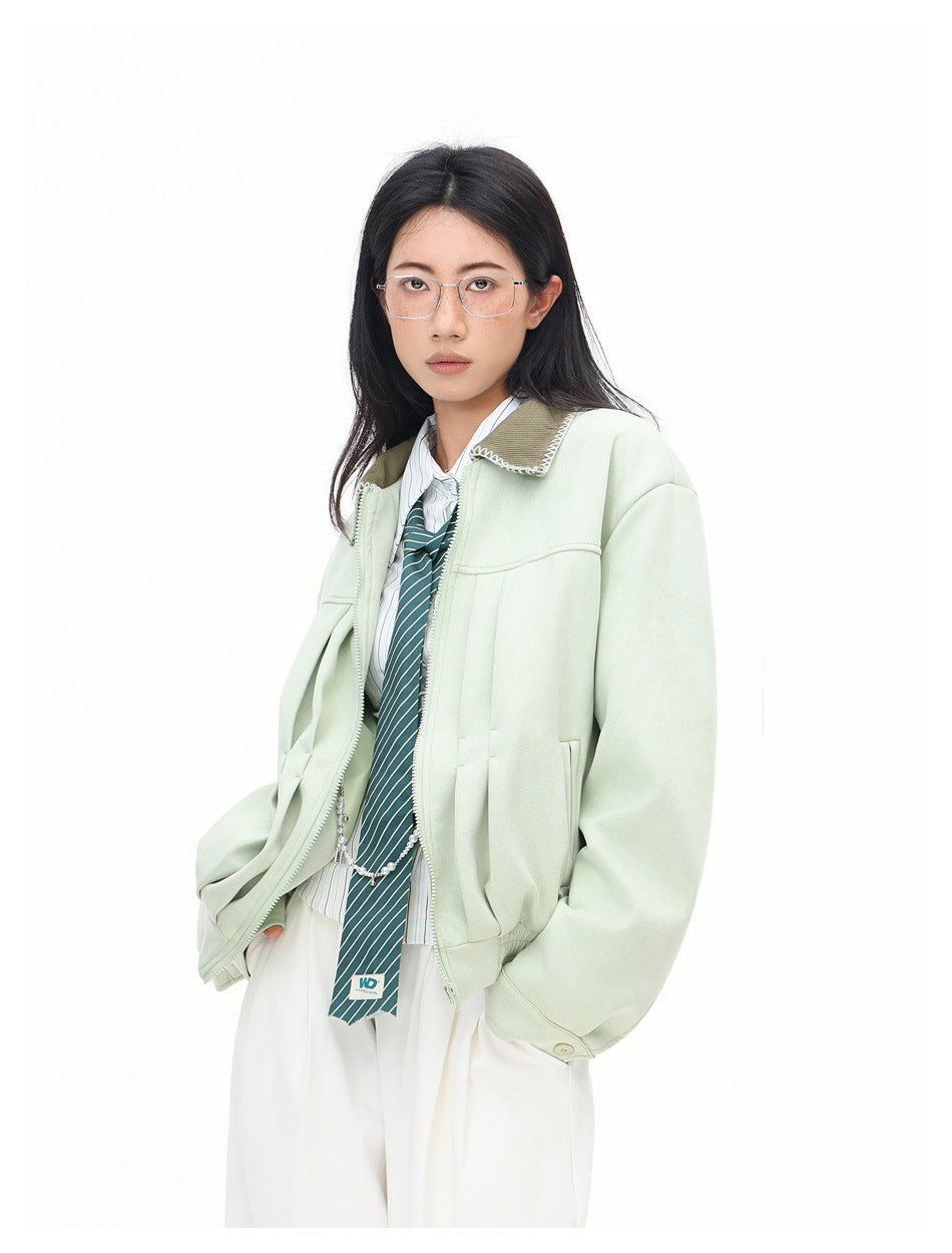 Model wearing mint green zip jacket with olive collar over striped shirt and green tie, hands in pockets