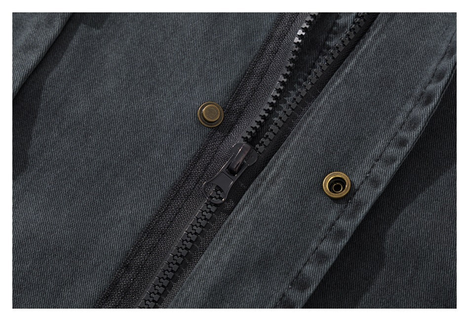 Close-up of a charcoal jacket's black zipper and brass-colored snap fasteners.