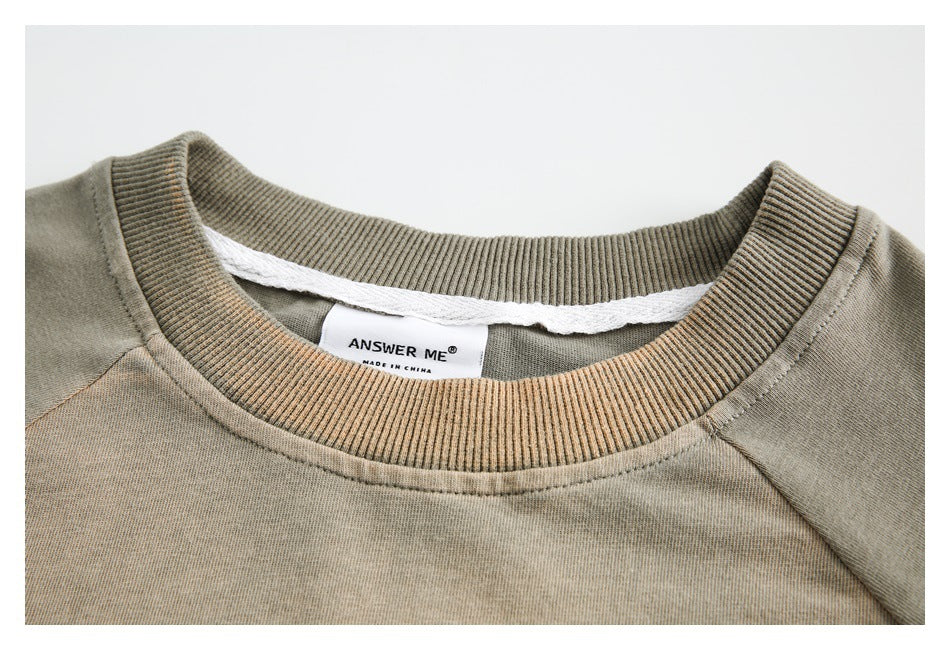 Close-up of a muted khaki crewneck collar with ribbed trim and a white ANSWER ME neck label.