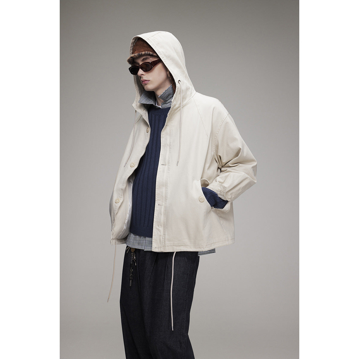 Model wearing an off-white hooded jacket with drawstrings and buttons over a navy sweater.