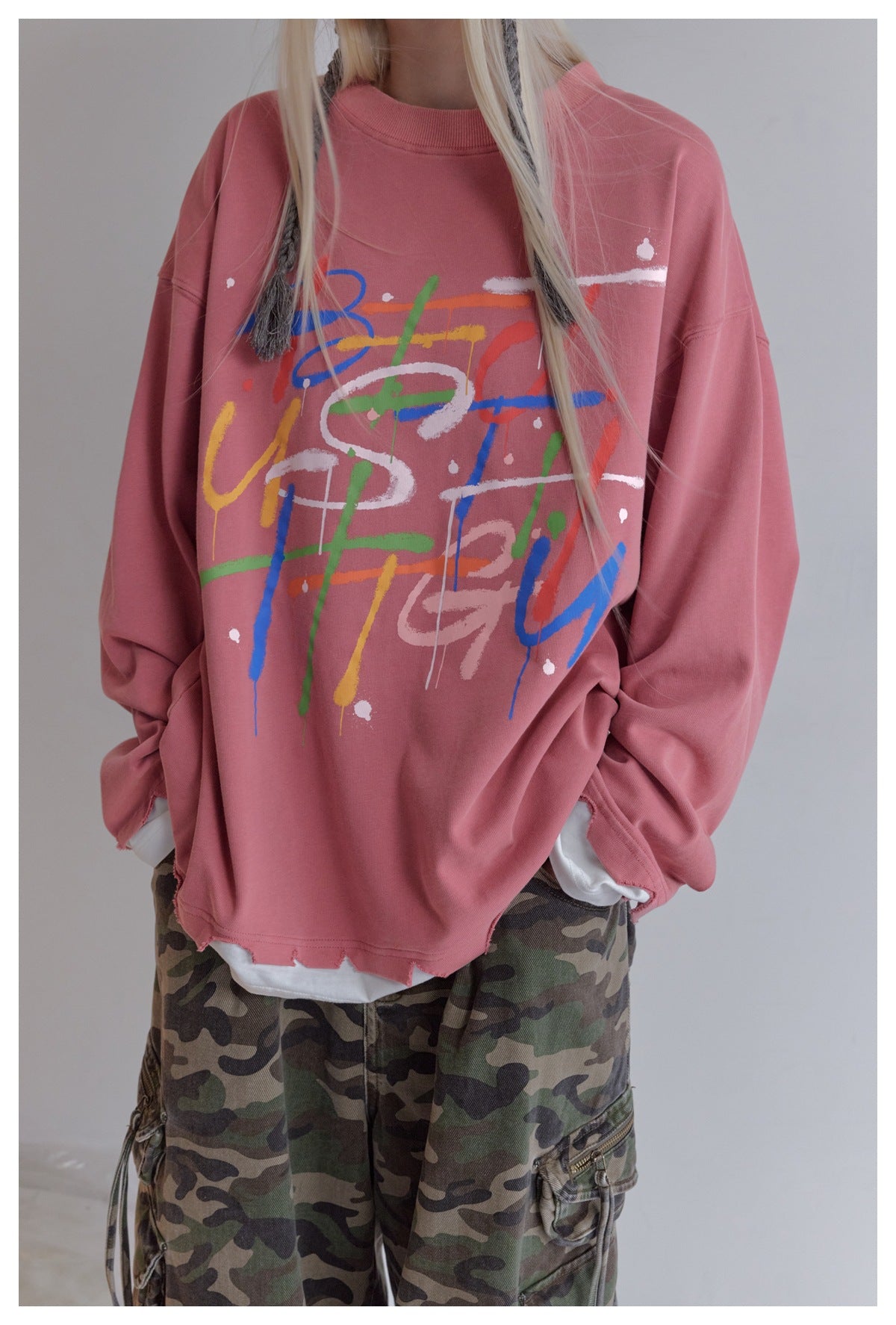 Close view of model wearing pink long-sleeve top with multicolor graffiti print and frayed hem over white layer