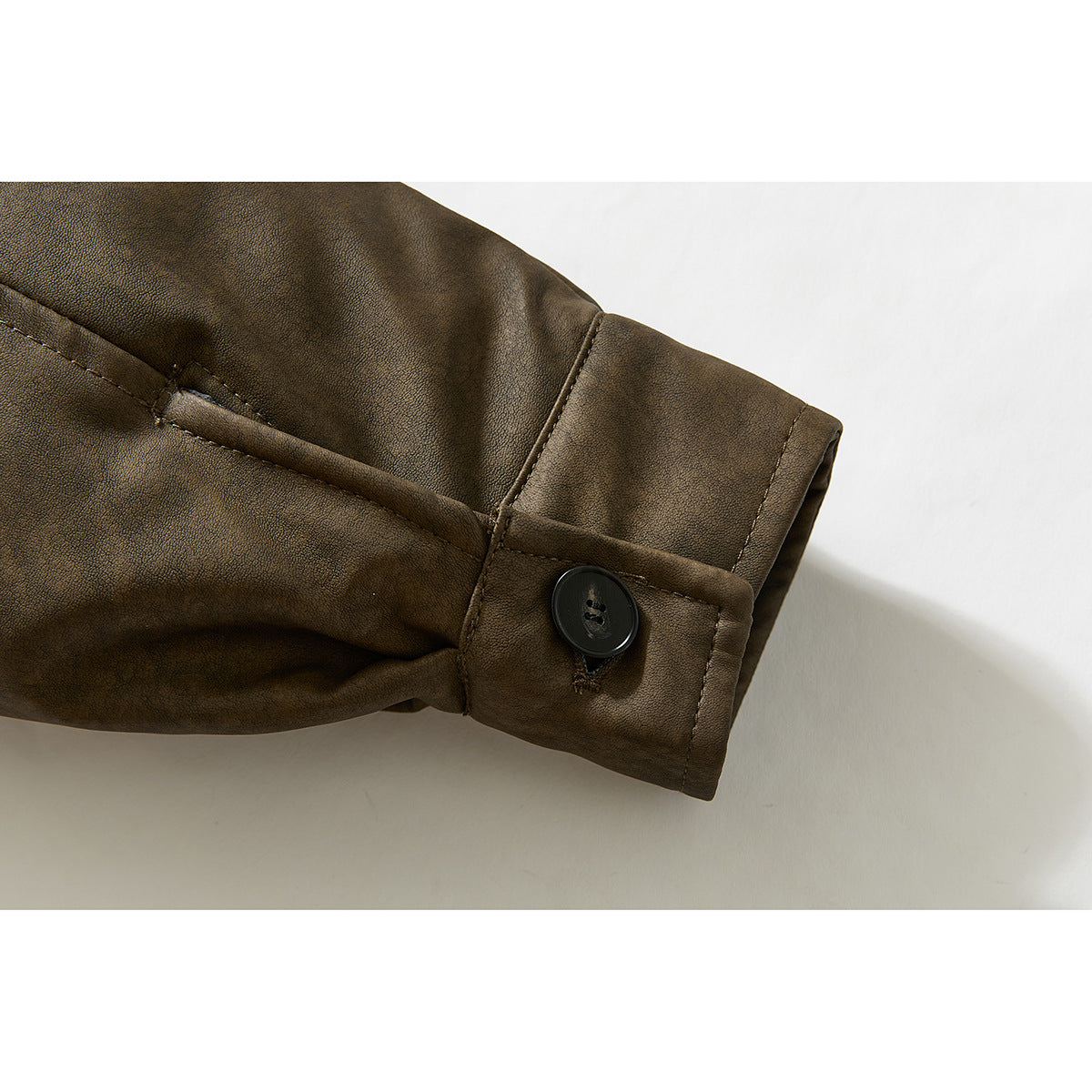 Close-up of a brown jacket sleeve cuff with a black button and stitched button tab.