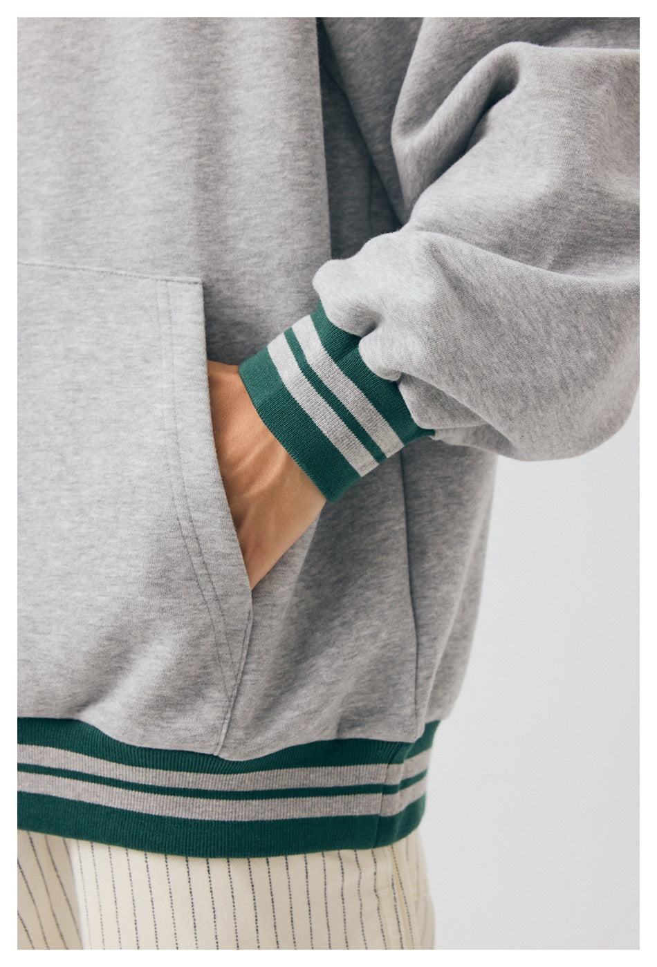 Close-up of a gray hoodie’s kangaroo pocket, sleeve, and green-and-gray striped cuff and hem.