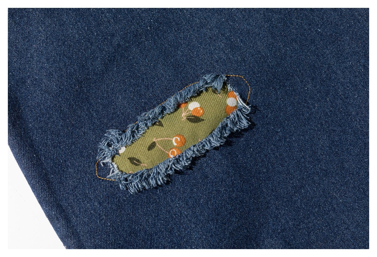 Close-up of a frayed green floral fabric insert on dark blue denim.