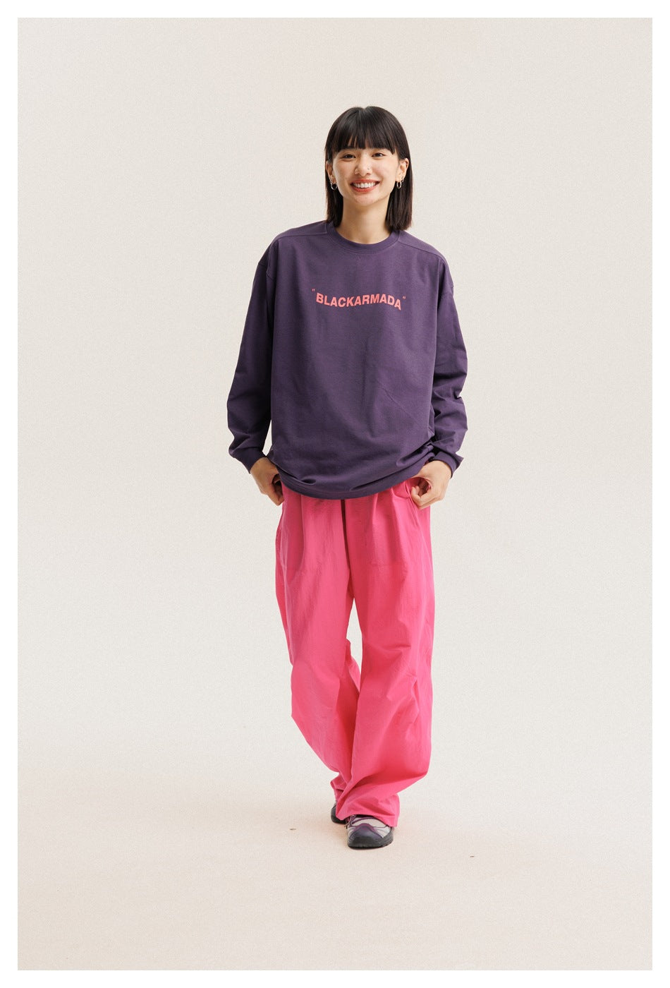 Full-length front view of a model wearing a plum graphic long-sleeve T-shirt and loose bright pink pants.