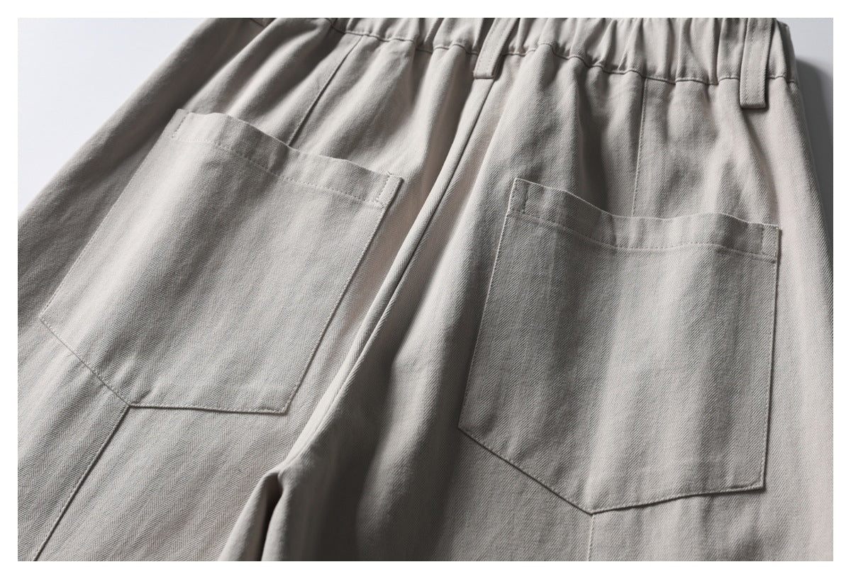 Close-up of light gray-beige trousers showing two large patch pockets, belt loops and a gathered waistband.