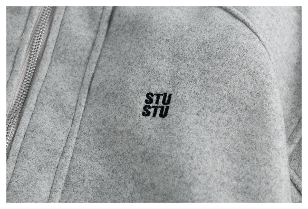 Close-up of a small black embroidered “STU STU” logo on the gray jacket.