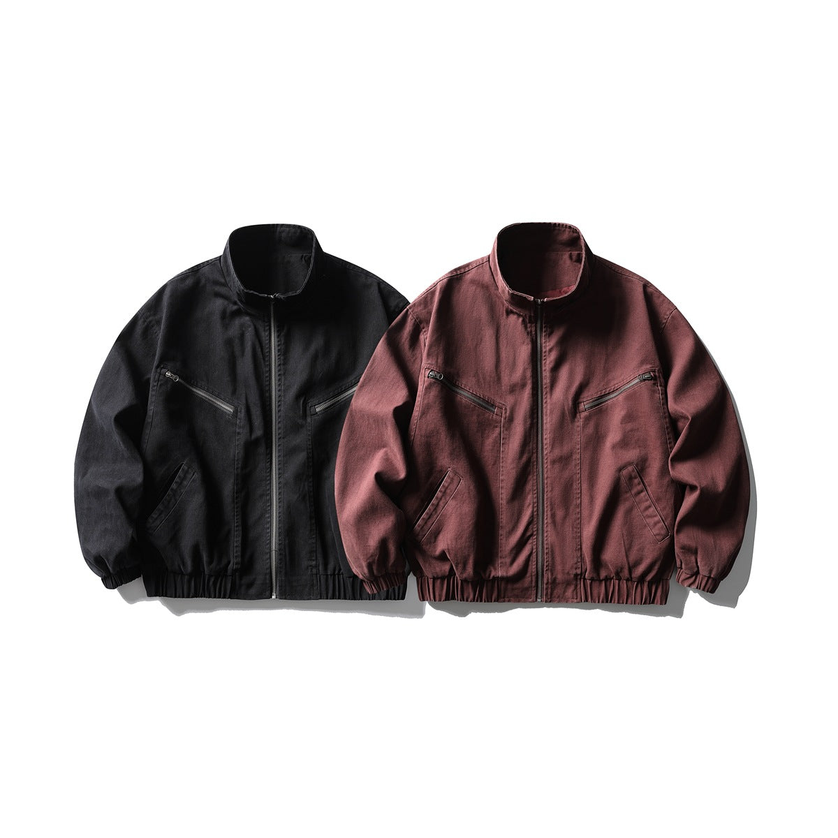 Front view of two zip-front jackets, one black and one burgundy, with stand collars and multiple pockets.