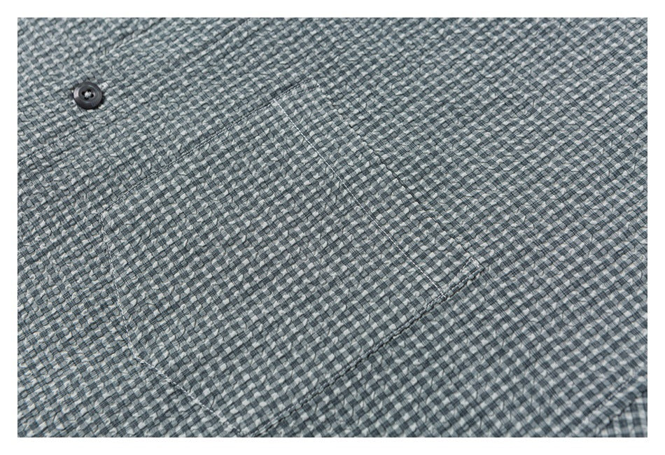 Close-up of gray check shirt fabric with a dark button and stitched pocket detail.