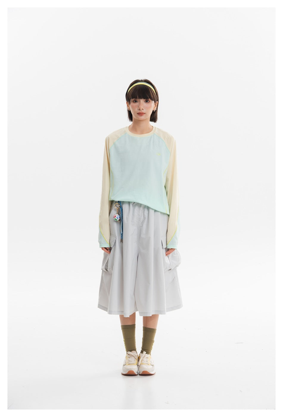 A woman models a pale mint shirt with cream sleeves and wide light-gray culottes against a white background.
