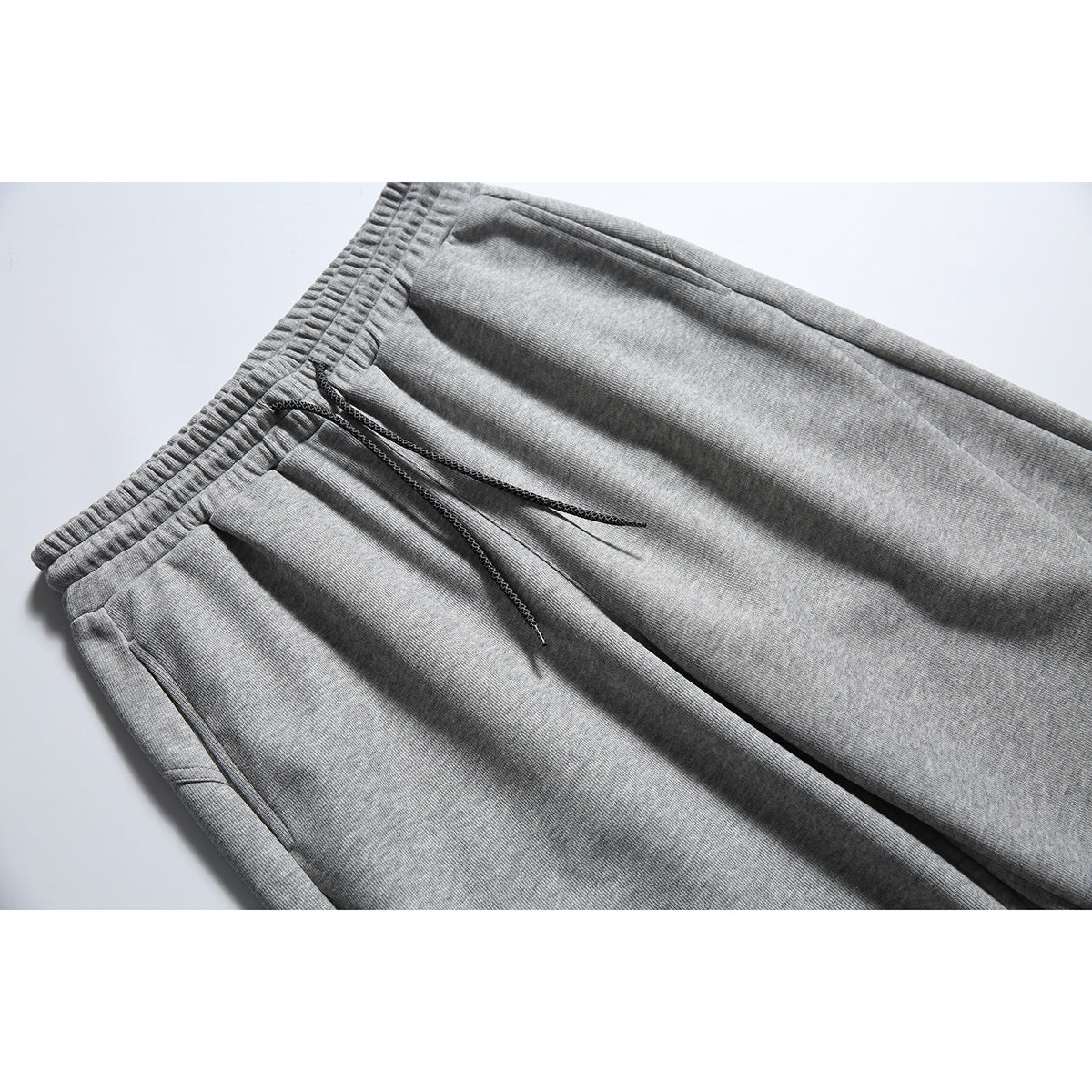 Close-up of heather gray sweatpants showing the elastic drawstring waist and a slanted side pocket.