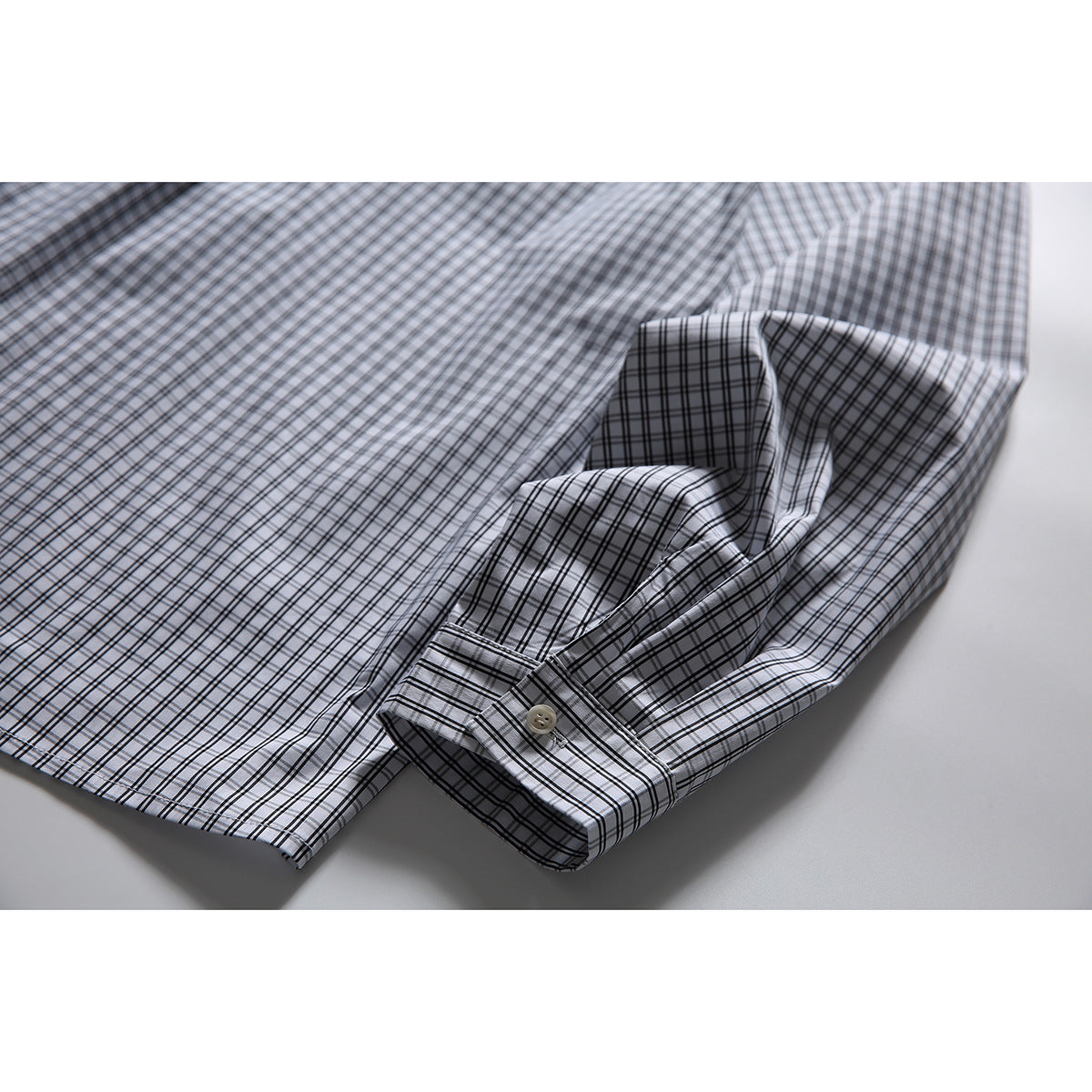 Close-up of the checked shirt's long sleeve and buttoned cuff on a light background.