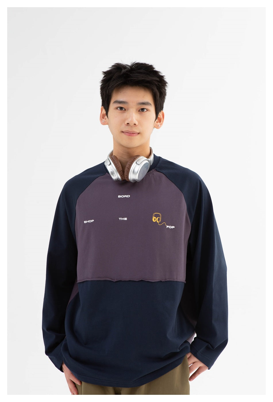 Model wearing a navy and muted purple color-block raglan sweatshirt with small white text and yellow headphone artwork on the