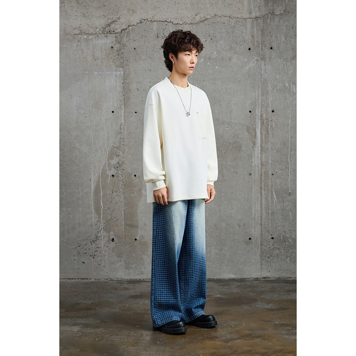 Full-length view of a model in an oversized white crewneck sweatshirt with a chest pocket and blue checked wide-leg trousers.