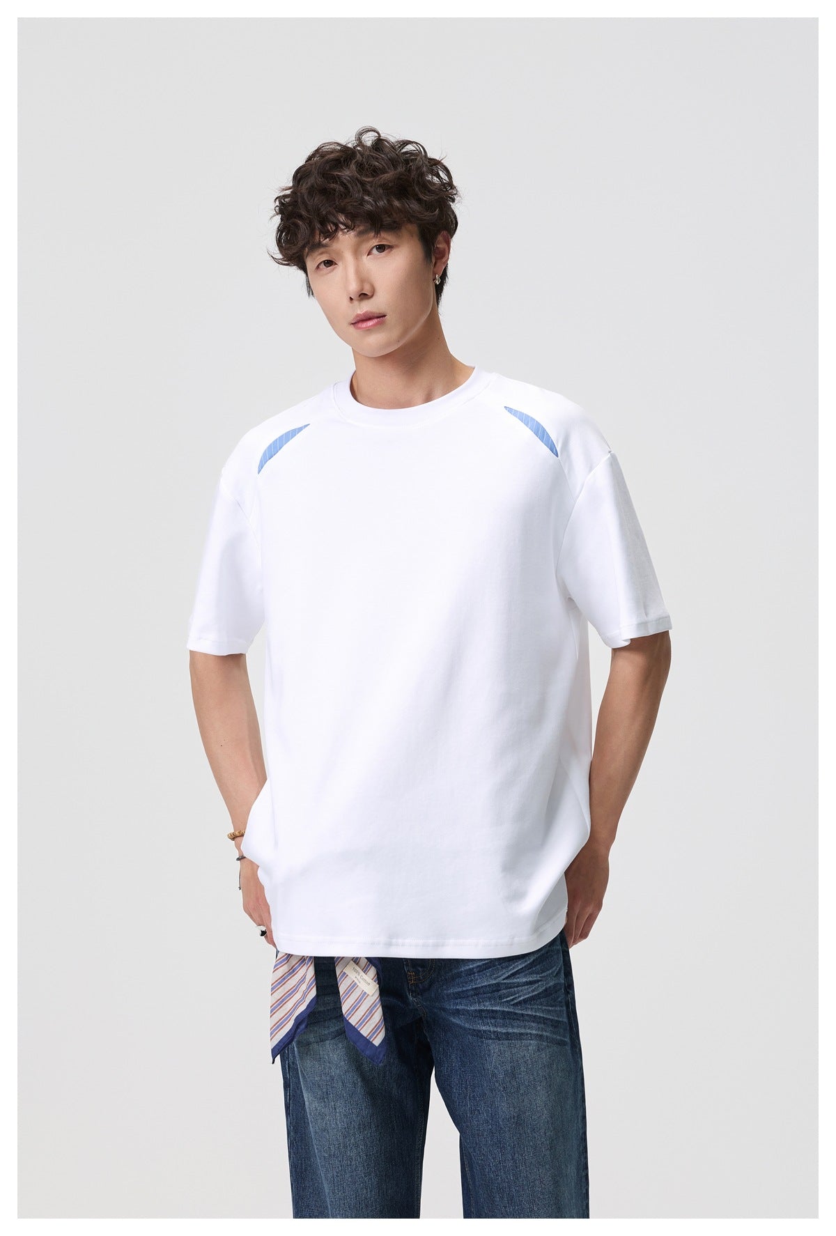 Closer front view of a model in a white oversized T-shirt with blue shoulder accents and blue jeans.