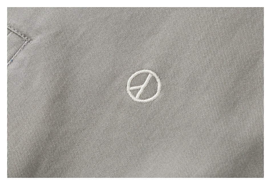 Close-up of a small white embroidered circular emblem on the gray jacket.