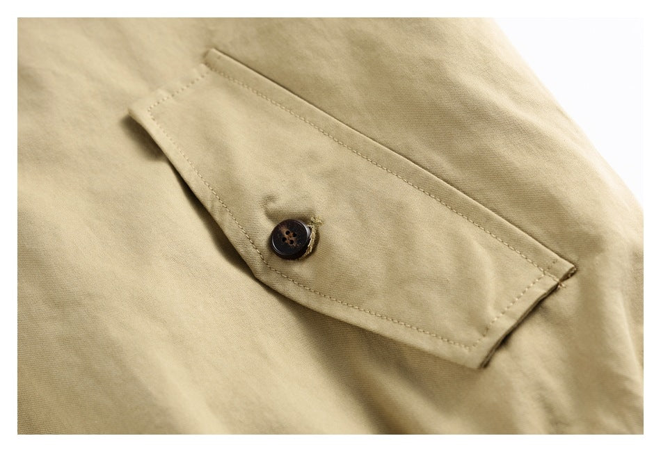 Close-up of a beige garment's buttoned flap pocket with neat topstitching.