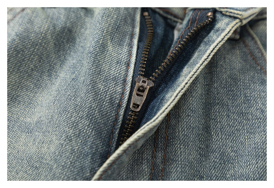 Close-up of the jeans' metal zipper and surrounding faded denim and stitching.