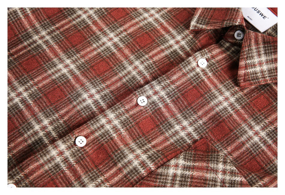 Close-up of the red-brown plaid fabric, white buttons, collar and chest pocket.