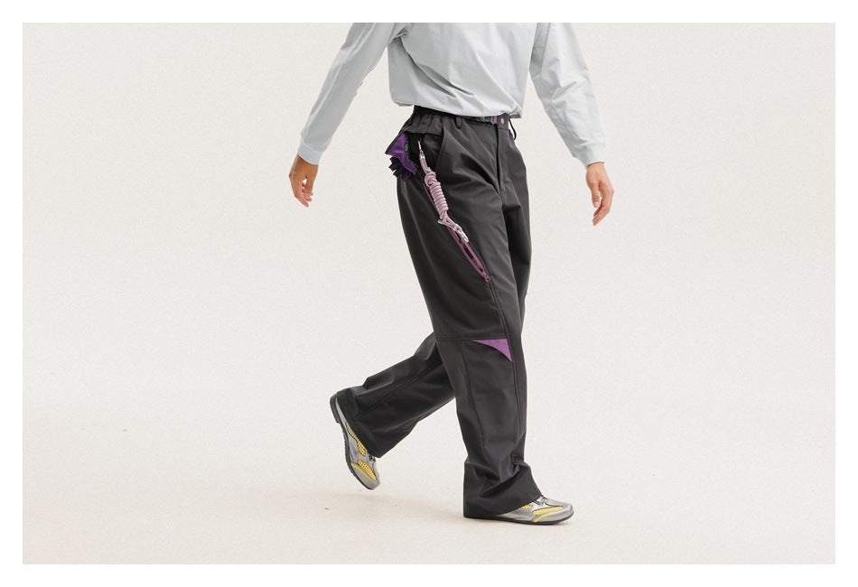 Model wearing loose black pants with purple knee accents and a purple clip-on strap, shown in a walking pose.